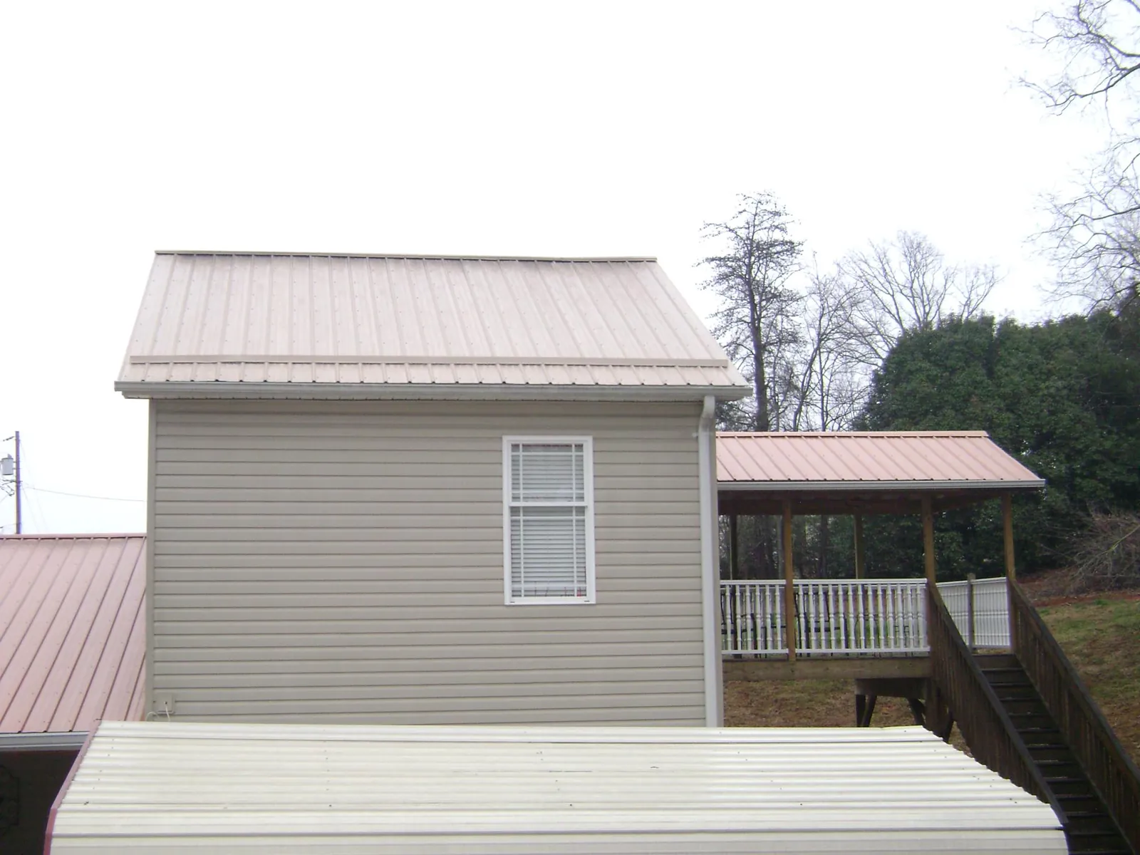 Tan metal roofs on a two story addition and attached porch, from a Roof Replacement job in Bethel